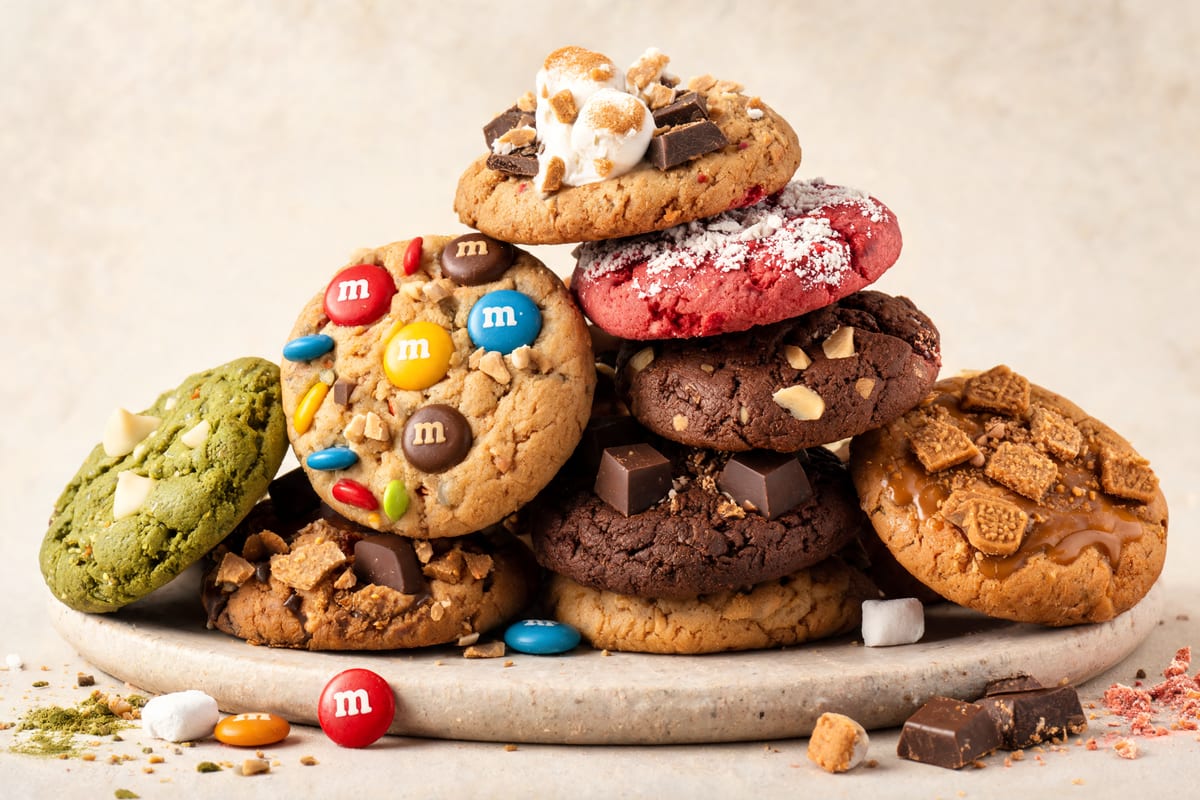 Tall stack of freshly baked Eva Bakes cookies, including M&M's, matcha, red velvet, double chocolate and salted caramel flavours