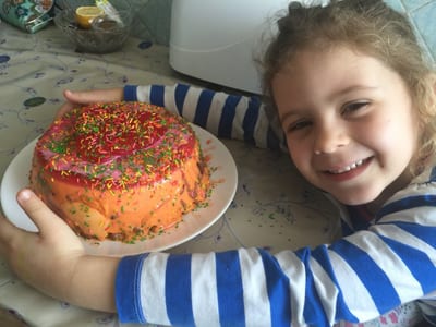 Evelina's six-year-old little sister proudly holding a homemade sprinkle cake